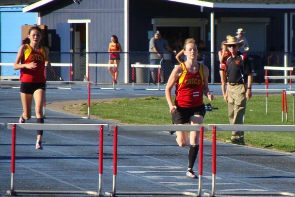 Chico's Lindsey Lundberg, seen here approaching the penultimate hurdle, while leading in the varsity girls 300m race. Coach Chuck Shelley and teammate Gabriella Mace are in the background.